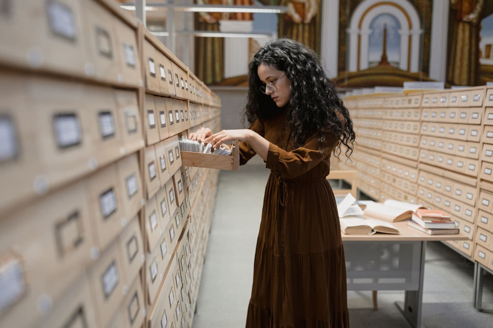 A researcher pulling a drawer from a library card catalog, searching printed index cards by hand.